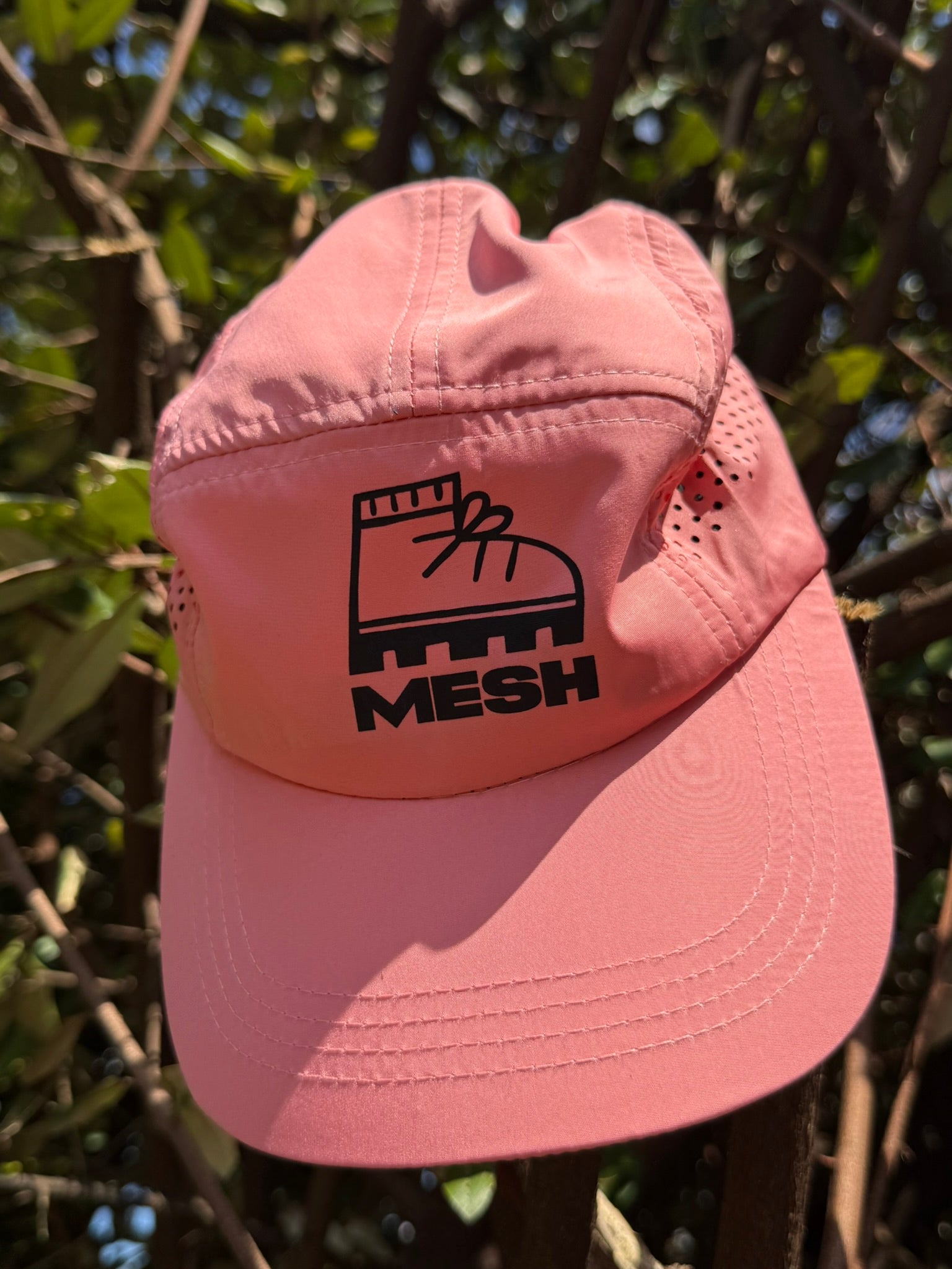 A pink athletic hiking cap with the MESH logo on the front, featuring a brim, eyelets, and an adjustable strap.